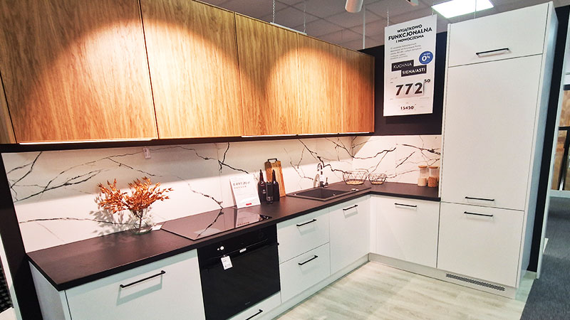 L-förmige Küche mit unterer Einbauweise in Weiß und einer schwarzen Arbeitsplatte sowie Hängeschränken im Holzstil.