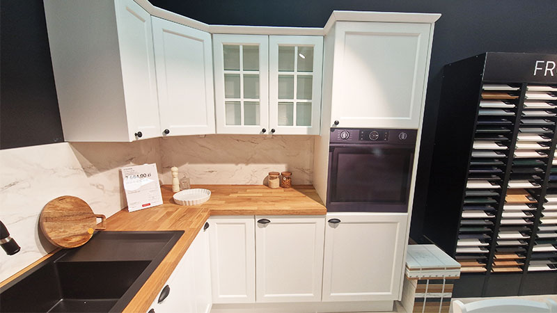 Schöne Eckküche mit Holzarbeitsplatte und hellen Fronten im klassischen Stil, mit einer verglasten Schranktür in der Mitte.